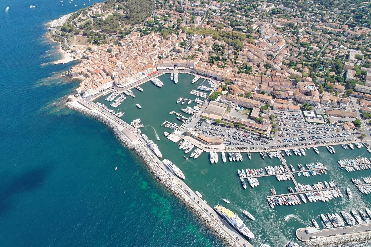 Saint-Tropez from the air in summer: the old port and its yachts, the harbor wall, the village roofs and the Gulf of Saint-Tropez